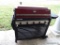 (OUT) CAPT'N COOK BARBEQUE GRILL; RED AND BLACK METAL GAS GRILL WITH FOLD UP SIDE AREAS AND 5