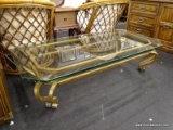 (R3) GLASS TOP COFFEE TABLE. CLEAR GLASS COFFEE TABLE ON A GOLD-TONED IRON BASE WITH SCROLL FEET.