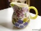 (SHELVES) HAND PAINTED FLORAL PITCHER WITH A YELLOW RIM AND HANDLE.