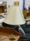 (R2) TABLE LAMP WITH A BRASS BASE AND CREAM COLORED COOLIE SHADE WITH DRAPING ACCENTS. APPEARS TO BE