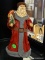 SANTA FIGURINE; CLOTH AND CERAMIC SANTA HOLDING A CHRISTMAS TREE AND A BAG OF GIFTS ON HIS BACK.