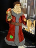 SANTA FIGURINE; CLOTH AND CERAMIC SANTA HOLDING A CHRISTMAS TREE AND A BAG OF GIFTS ON HIS BACK.