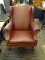 BURGUNDY UPHOLSTERED OFFICE ARM CHAIR WITH BRASS STUDDING AND MAHOGANY BASE. MEASURES 29 IN X 34 IN