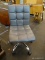 MODERN ROLLING CHAIR WITH GRAY UPHOLSTERY AND BUTTON TUFTED SEAT AND BACK. MEASURES 17 IN X 19 IN X