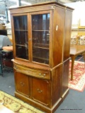 CHINA CABINET WITH 2 INTERIOR WOODEN SHELVES, A CENTER DRAWER, AND 2 LOWER DOOR THAT OPEN TO REVEAL