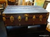 STEAMER TRUNK WITH LATCHING LOCK. IS BROWN AND BLACK IN COLOR WITH BRASS HARDWARE. MEASURES 34 IN X