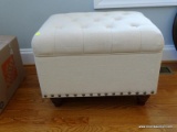 (LR) LIFT-TOP OTTOMAN WITH CREAM COLORED UPHOLSTERY AND BRASS RIVETING AROUND THE BOTTOM EDGE.
