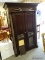 MAHOGANY FINISH 2 DOOR ARMOIRE WITH A SUN CARVED TOP, TWIST CARVED COLUMN CORNERS, CARVED FRONT
