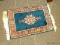 SMALL AREA RUG IN HUES OF RED, BLUE, AND CREAM. MEASURES 1 FT 6 IN X 2 FT 2 IN. ITEM IS SOLD AS IS