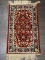 SMALL AREA RUG IN HUES OF RED, BLUE, AND CREAM. MEASURES 1 FT 4 IN X 2 FT 5 IN. ITEM IS SOLD AS IS