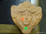 TERRA-COTTA WALL POCKET IN THE FORM OF A WOMAN'S FACE WITH A FLORAL HEADDRESS. MEASURES 9.5 IN X 3