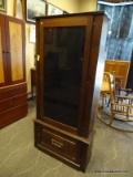 OAK GUN CABINET WITH 1 GLASS DOOR AND A LOWER OAK DOOR WITH METAL PULL. HAS A KEY (IS BENT BUT