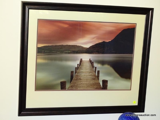 (LR) FRAMED AND DOUBLE MATTED PRINT OF A DOCK SCENE WITH MOUNTAINS AND A SUNSET IN THE BACKGROUND.
