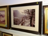 (R2) FRAMED PHOTOGRAPH OF A SNOWY MOUNTAIN-SIDE SCENE WITH THE SUN SHINING IN THROUGH THE CLOUDS.