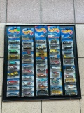 (LOCATED CENTER AISLE) HOT WHEELS CARS IN ORIGINAL PACKAGES IN BLACK DISPLAY RACK. MOSTLY 1990S