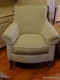 (LIBRARY) BEIGE ARM CHAIR WITH WALNUT LEGS RESTING ON BRASS CASTERS FROM THE JEFFERSON COLLECTION-
