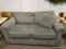 (R3) GRAY UPHOLSTERED LOVESEAT WITH AN ACCENT PILLOW. MEASURES 62 IN X 38 IN X 35 IN. ITEM IS SOLD