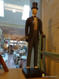 (R3) WOODEN STATUE OF A GENTLEMAN IN A SUIT WITH CANE. MEASURES 24.5 IN TALL. ITEM IS SOLD AS IS
