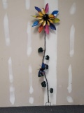 TALL METAL MULTI-COLORED SUNFLOWER YARD ORNAMENT WITH A BUTTERFLY AMING THE LEAVES ON THE STALK. THE