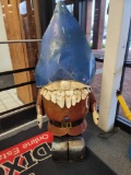 BENCHMADE METAL GNOME YARD ORNAMENT. HE IS WEARING A BLUE HAT AND A RED OUTFIT. MEASURES APPROX 25