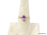 GOLD TONE ENGAGEMENT RING WITH AN APPROX. 1 CT. OVAL CUT PRONG SET SIMULATED AMETHYST STONE.