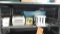 Lot on Shelf of Various Office Supplies: Hole Punch, Stapler, UPS Printers, Zip Disk