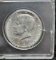 1964 Kennedy Half Dollar - hard plastic container, ungraded