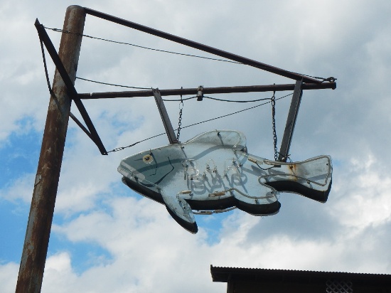 NEON FISH SIGN  HANGING ON POLE ON SIDE PARKING LOT OF BUILDING