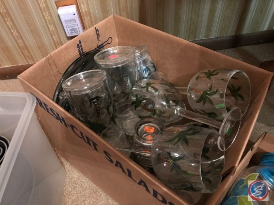 Box containing plastic palm tree design cups, wine glasses, plates, and more