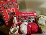 Box containing assorted Nebraska Husker memorabilia including a Husker no parking sign, husker caps,