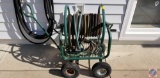 (2) garden hoses, metal hose winder with basket on wheels and some hose attachments