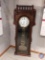 Grandfather clock w/ incised floral patterns. 5 wooden spindles on top. Large pendulum w/ harp shape
