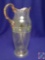 Opaque glass pitcher. 13? Shamrocks w/ horseshoes. Green & gold accents with red bead in center.