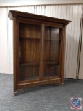 Brown oak library case w/ 2 glass front doors, 4 shelves, & 4 caster wheels. Carved squares at