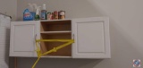 White wall cabinets with some cleaning supplies, can food, Cooler on wheels, work sink with various