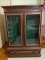 Vintage Wooden Gun Cabinet on Casters with Glass Front & Ornate Design