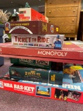 Stack of vintage board games including Monopoly, Ticket to Ride, NBA basket, etc.