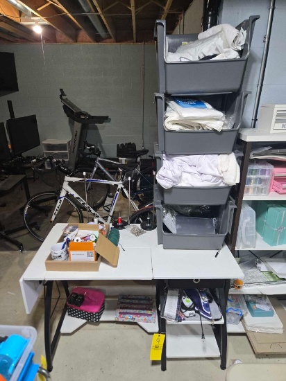 Sewing table, thread, stacked bins with material, iron, and more
